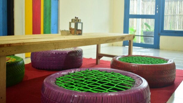 Una habitación con una mesa de madera, franjas verticales de colores en la pared y una ventana con vista a una valla.
