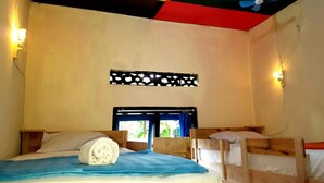 Una habitación con dos camas de madera, un ventilador de techo, una ventana con cortinas y una lámpara fijada a la pared.