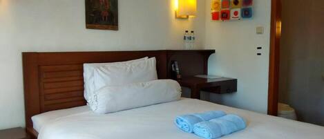 Une chambre d’hôtel avec une tête de lit en bois, du linge de lit blanc, un tableau au mur, une table de chevet avec une lampe et un téléphone fixé au mur.