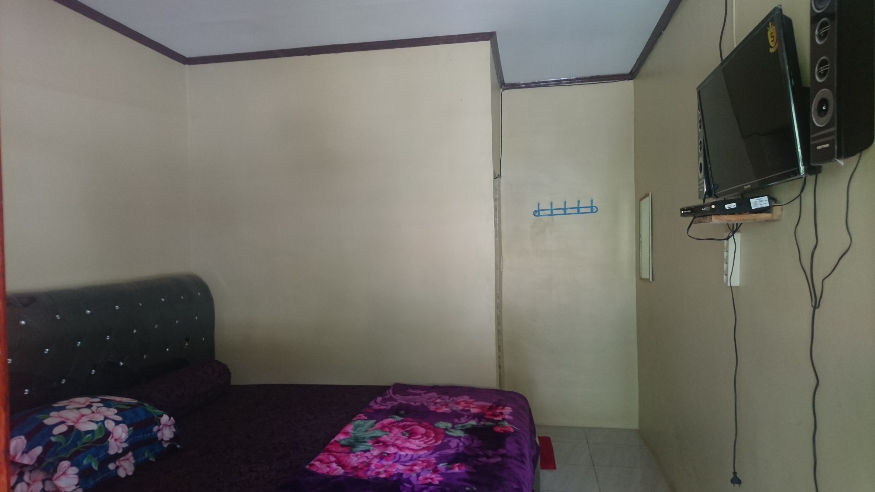 A small, simple room with a bed, a television mounted on the wall, and a power outlet.