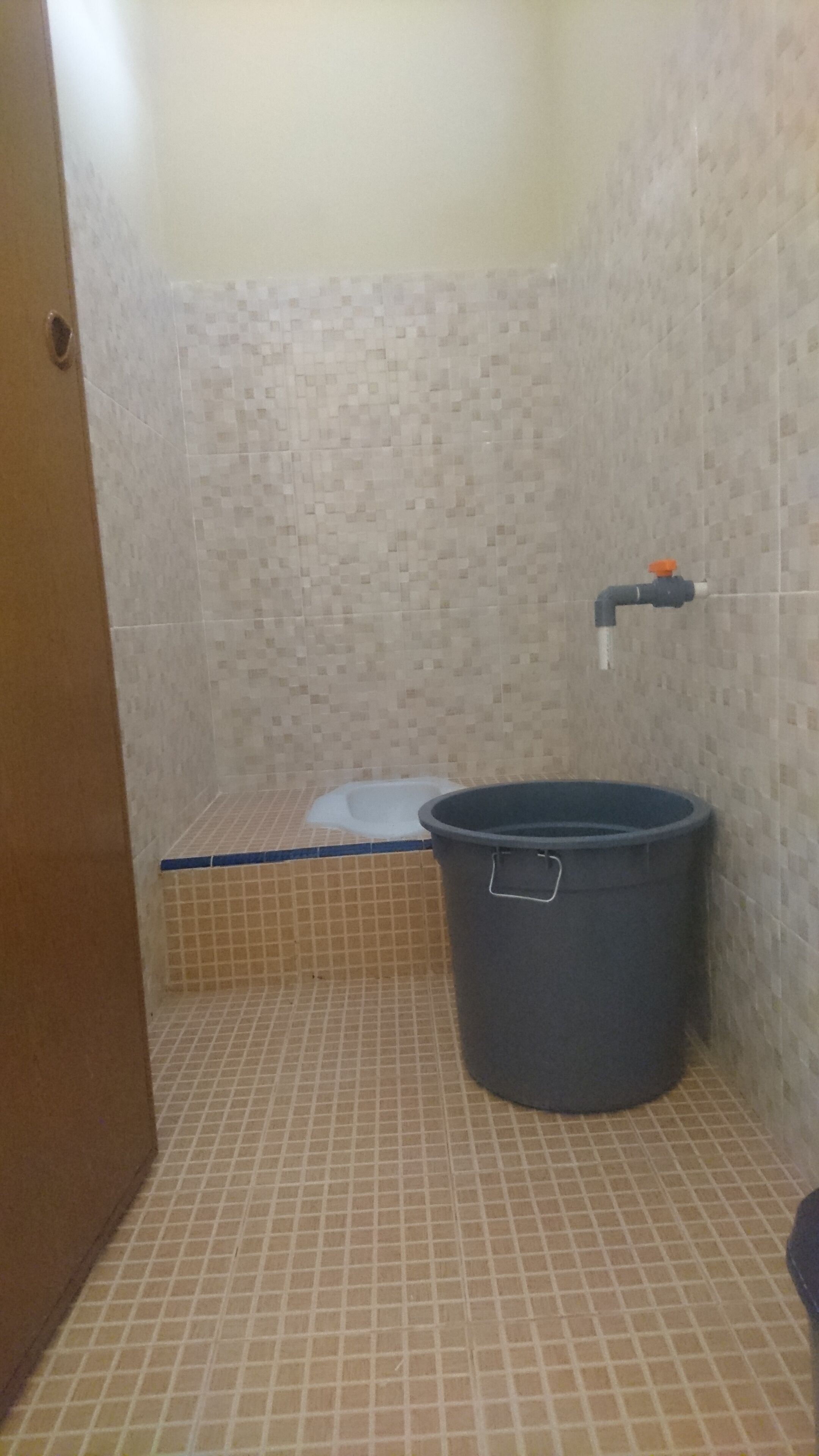 Un baño pequeño con inodoro, un balde y zona de ducha.