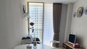 Ein modernes Wohnzimmer mit Esstisch, einer Couch, einem Fernseher auf einem Schrank und einem großen Fenster mit Vorhängen.