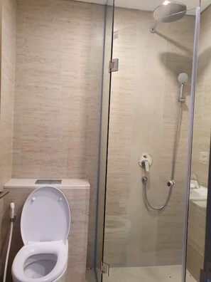 A bathroom with a glass-enclosed shower, a toilet, and a sink. - Pamengkang Apartment @Taman Anggrek Residence (Jakarta)