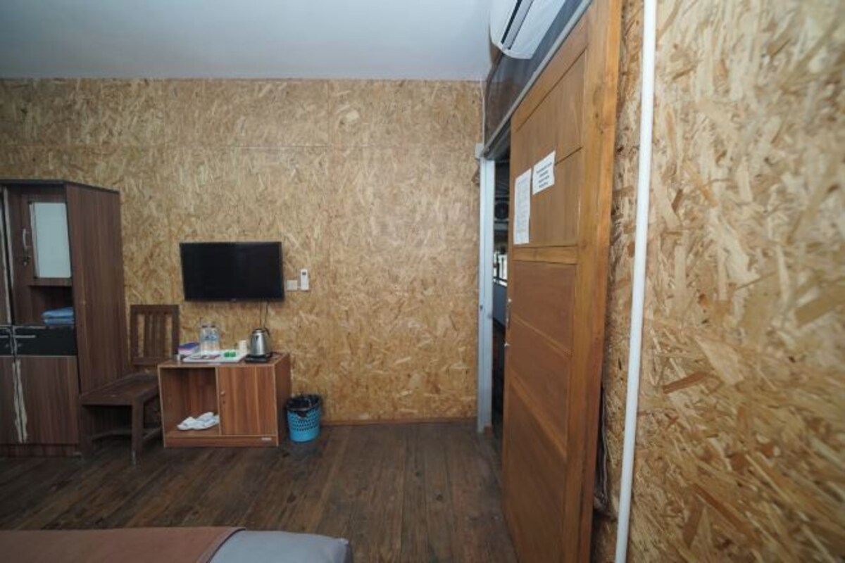 A small room with a wooden floor, a wooden cabinet, a television mounted on the wall, and a door with a sign.