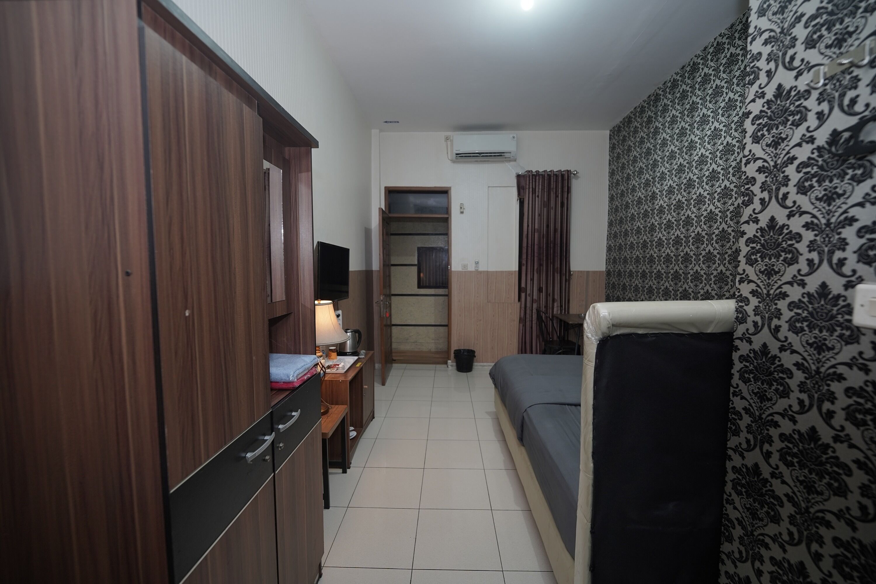 Habitación pequeña con cama, armario, escritorio con lámpara y televisión.