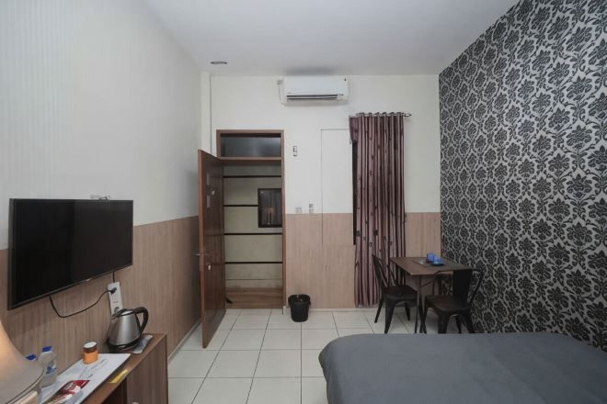 A hotel room with a bed, a desk with a TV, a wardrobe, a small table, and a patterned wall.