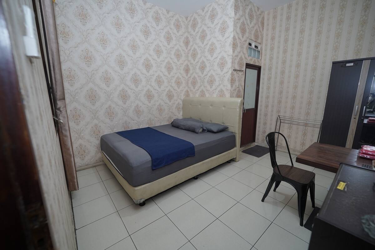 A bedroom with a bed, a chair, a table, and a wardrobe.