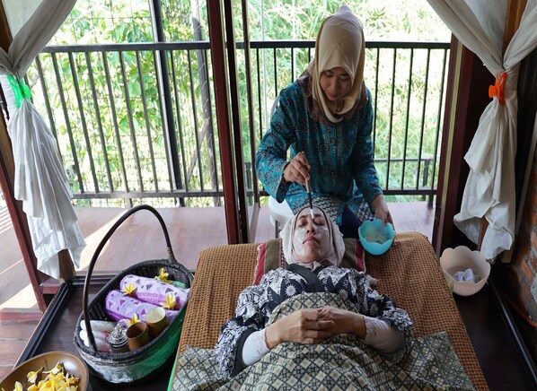 A person receiving a facial treatment on a massage table with a basket of towels and a bowl of water nearby. - NILA HOUSE, Sharia Family Home Stay (Jakarta)