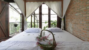A room with a bed, white bedding, a basket with flowers, and a view of greenery through large windows. - NILA HOUSE, Sharia Family Home Stay (Jakarta)