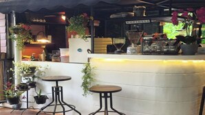 An outdoor seating area with a white counter, metal stools, and hanging plants. - NILA HOUSE, Sharia Family Home Stay (Jakarta)