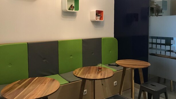 A modern seating area with green and grey cushioned benches, wooden tables, and wall-mounted planters. - The Colour Hostel (Pontianak)