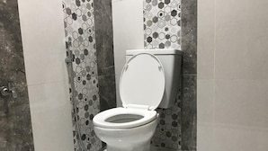 A toilet with a closed lid in a bathroom with patterned tiles and a tiled floor. - The Colour Hostel (Pontianak)