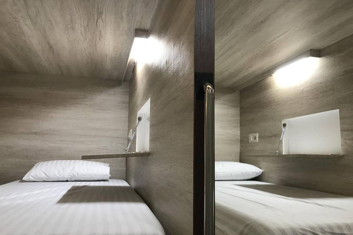 A compact room with two beds, a wooden ceiling, and a small window.