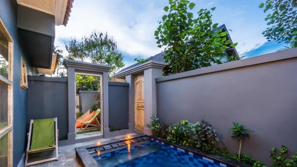 A modern outdoor swimming pool area with a stone-tiled deck, a lounge chair, and a small garden with plants and a palm tree. - Kawans Inn Lembongan (Lembongan Island)