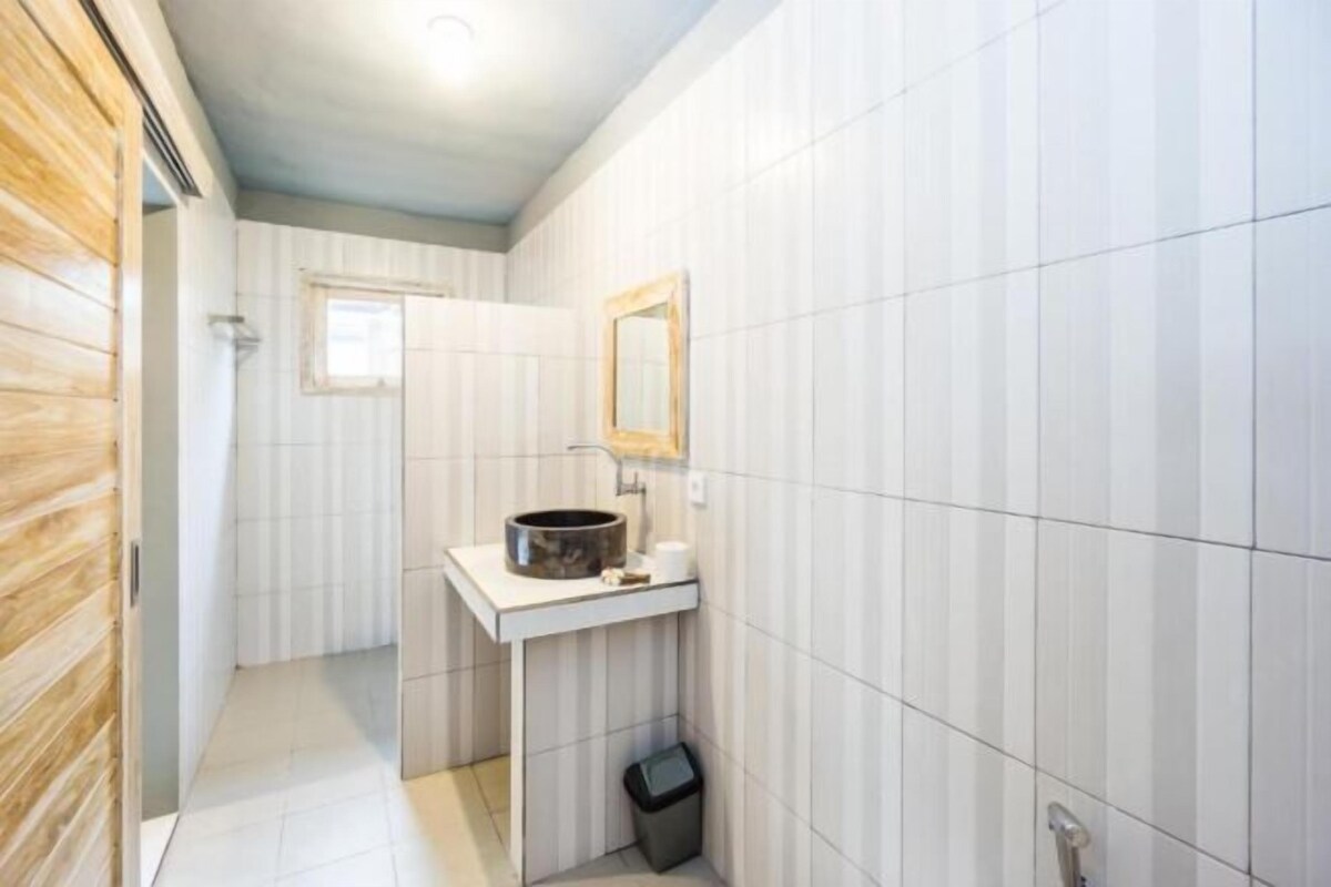 A bathroom with white tiled walls, a wooden door, a sink with a mirror, and a small window.
