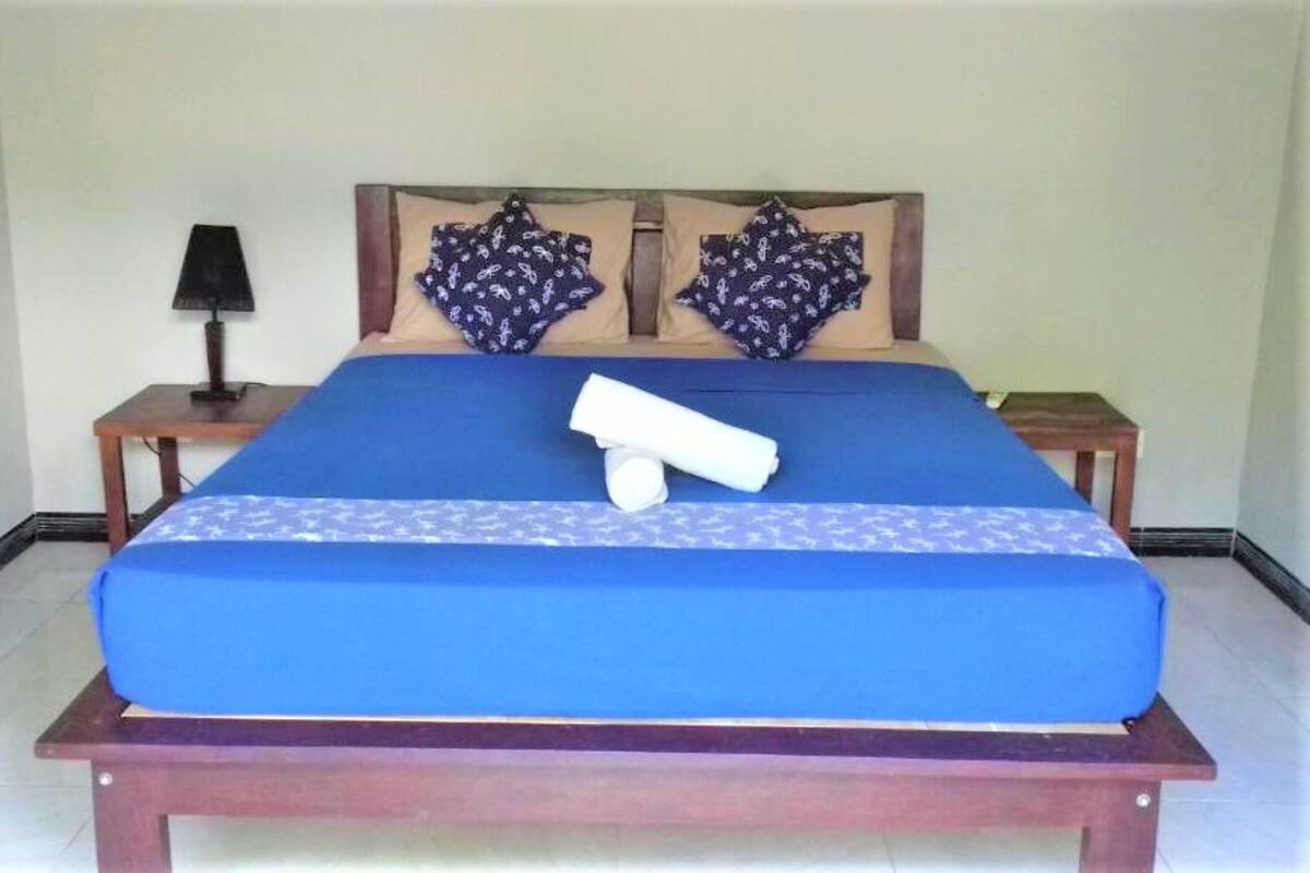 A bed with a blue mattress, two pillows with a floral pattern, and a rolled towel on the bed.