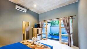 A hotel room with a bed, a small desk, a TV, and a sliding glass door to a pool area. - Kawans Inn Lembongan (Lembongan Island)
