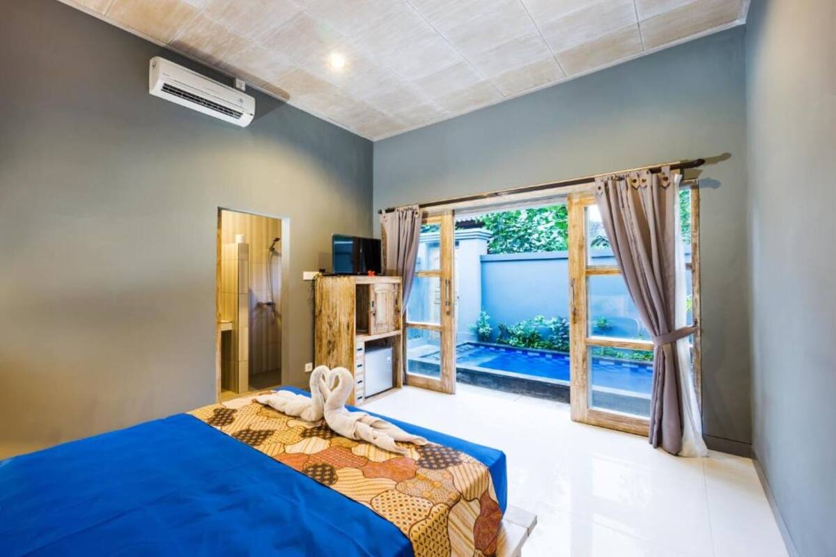 A hotel room with a bed, a small desk, a TV, and a sliding glass door to a pool area.