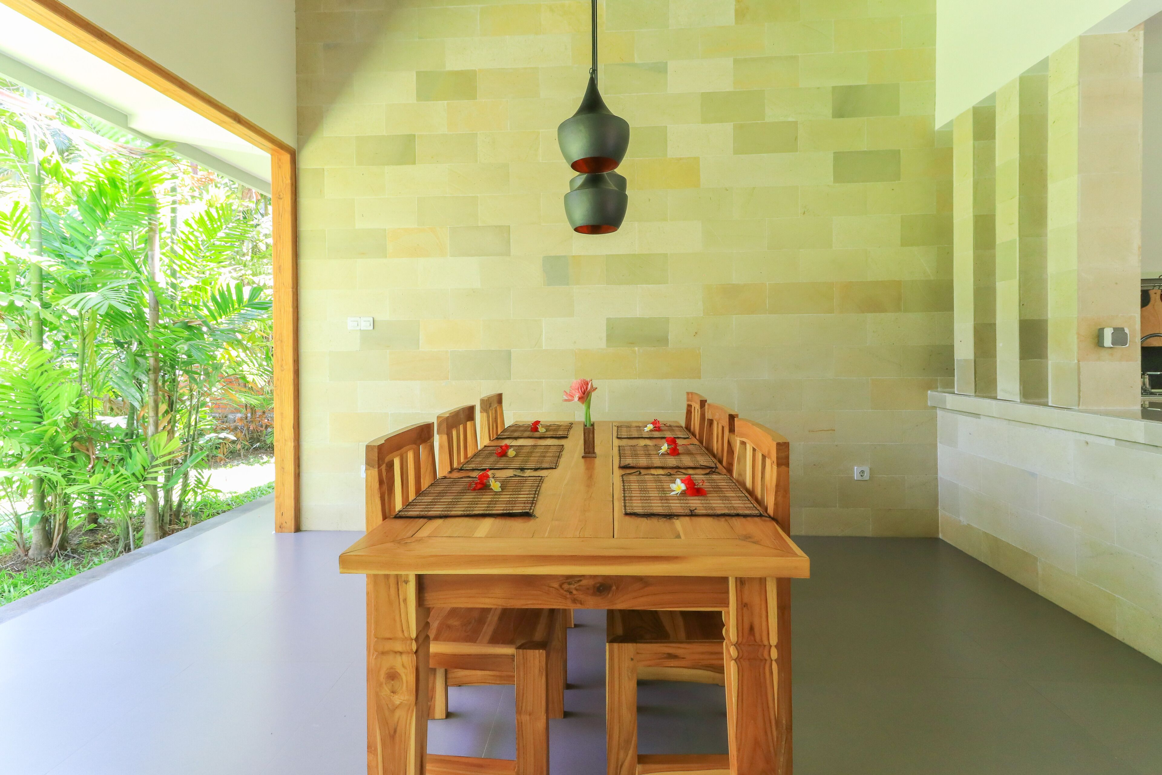 Un comedor con mesa y sillas de madera, una lámpara colgante y vistas al exterior con vegetación.