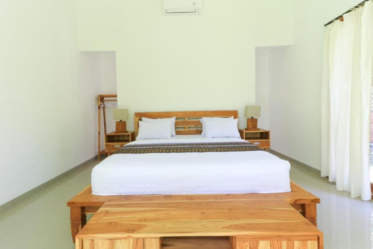 Quarto bem arrumado com cama de madeira, mesas de cabeceira e um banco de madeira.