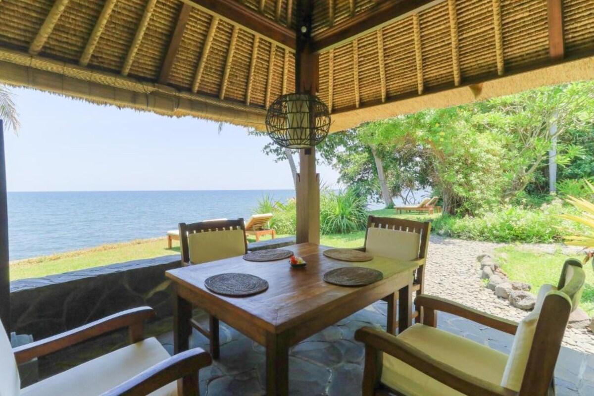 A wooden table with four chairs, a hanging light fixture, and a view of the ocean.