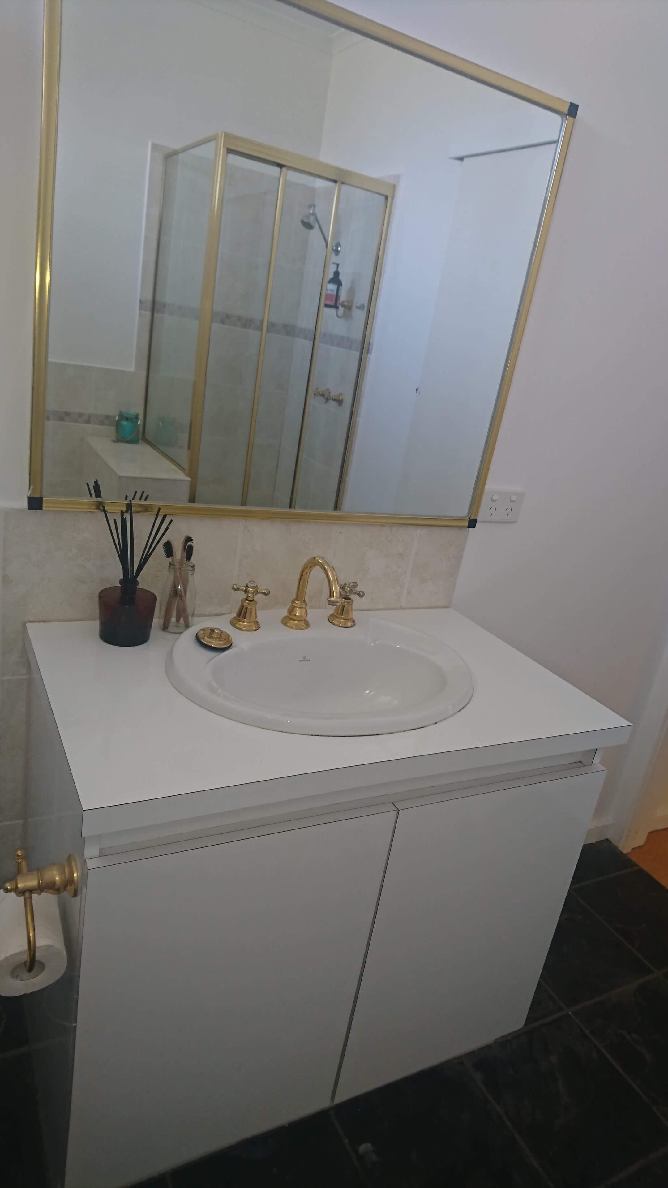 Un baño con lavamanos blanco, grifos dorados y un espejo grande encima.