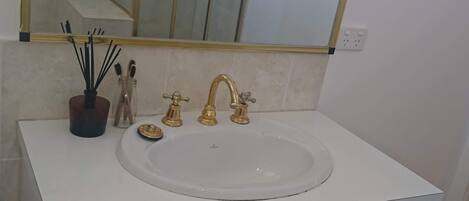 Un baño con lavamanos blanco, grifos dorados y un espejo grande encima.