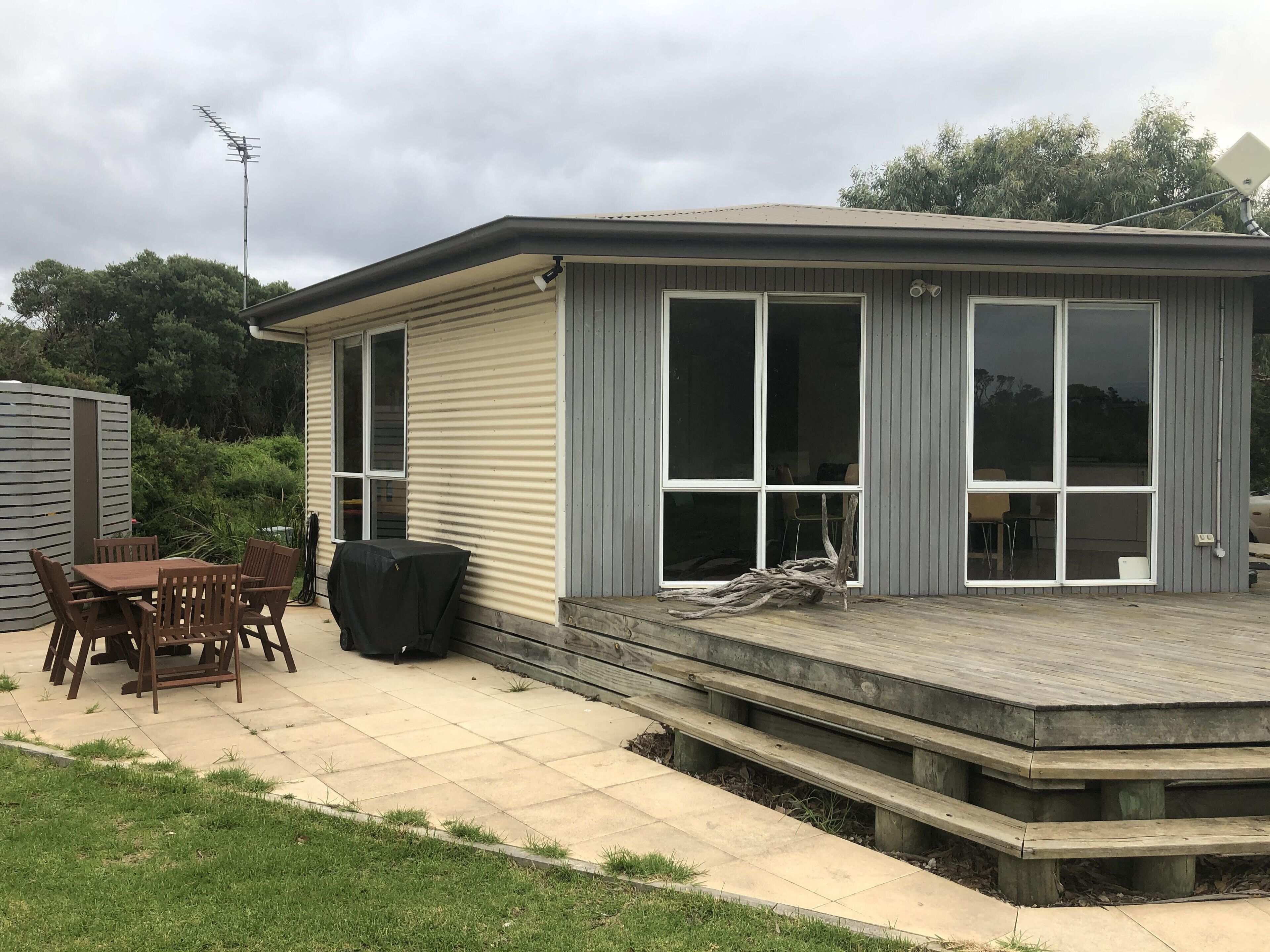 A single-story house with a patio, a covered table, and chairs.