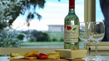 A bottle of Windy Peak Pinot Grigio King Valley 2017 wine, two empty wine glasses, and a wooden board with bread, tomatoes, and cheese.