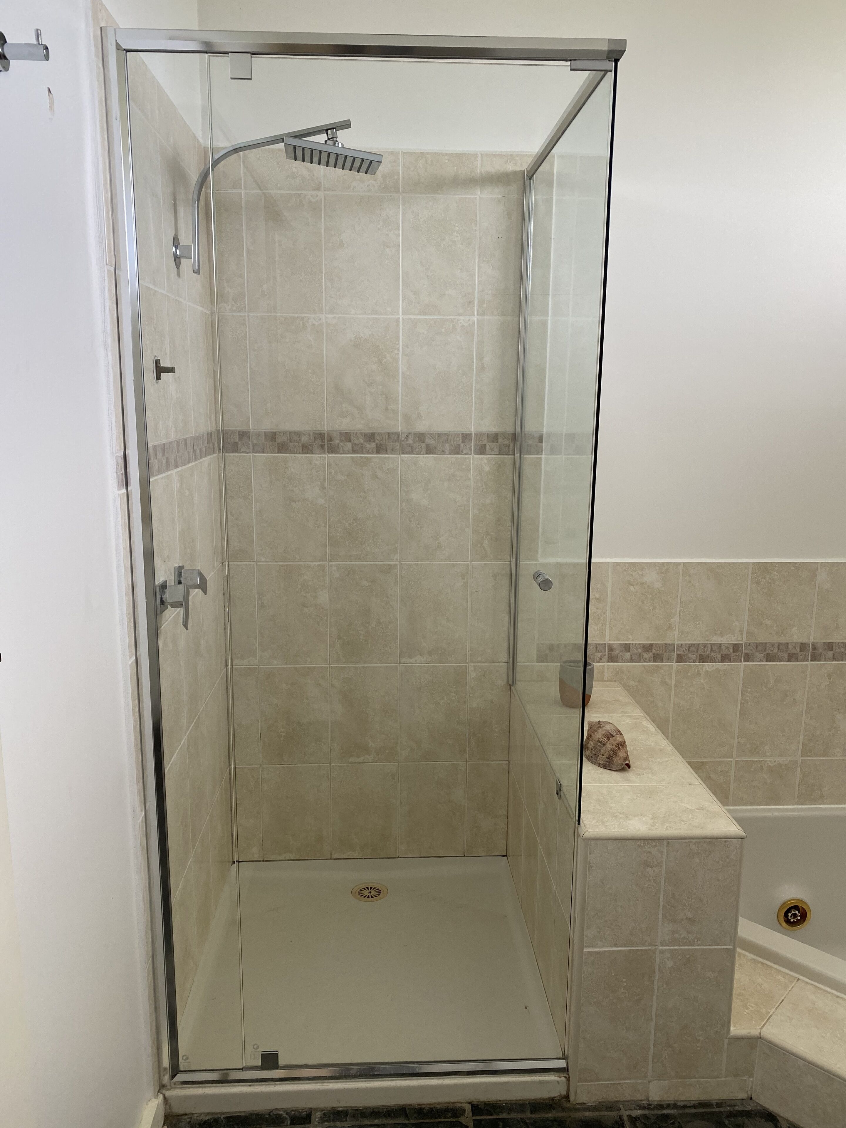 A glass-enclosed shower with beige tiles and a small shelf.