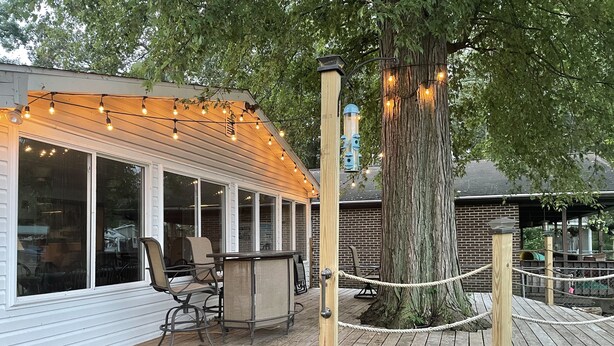 Eine Holzterrasse mit Sitzgelegenheiten im Freien, Lichterketten und einer Seilbrüstung.