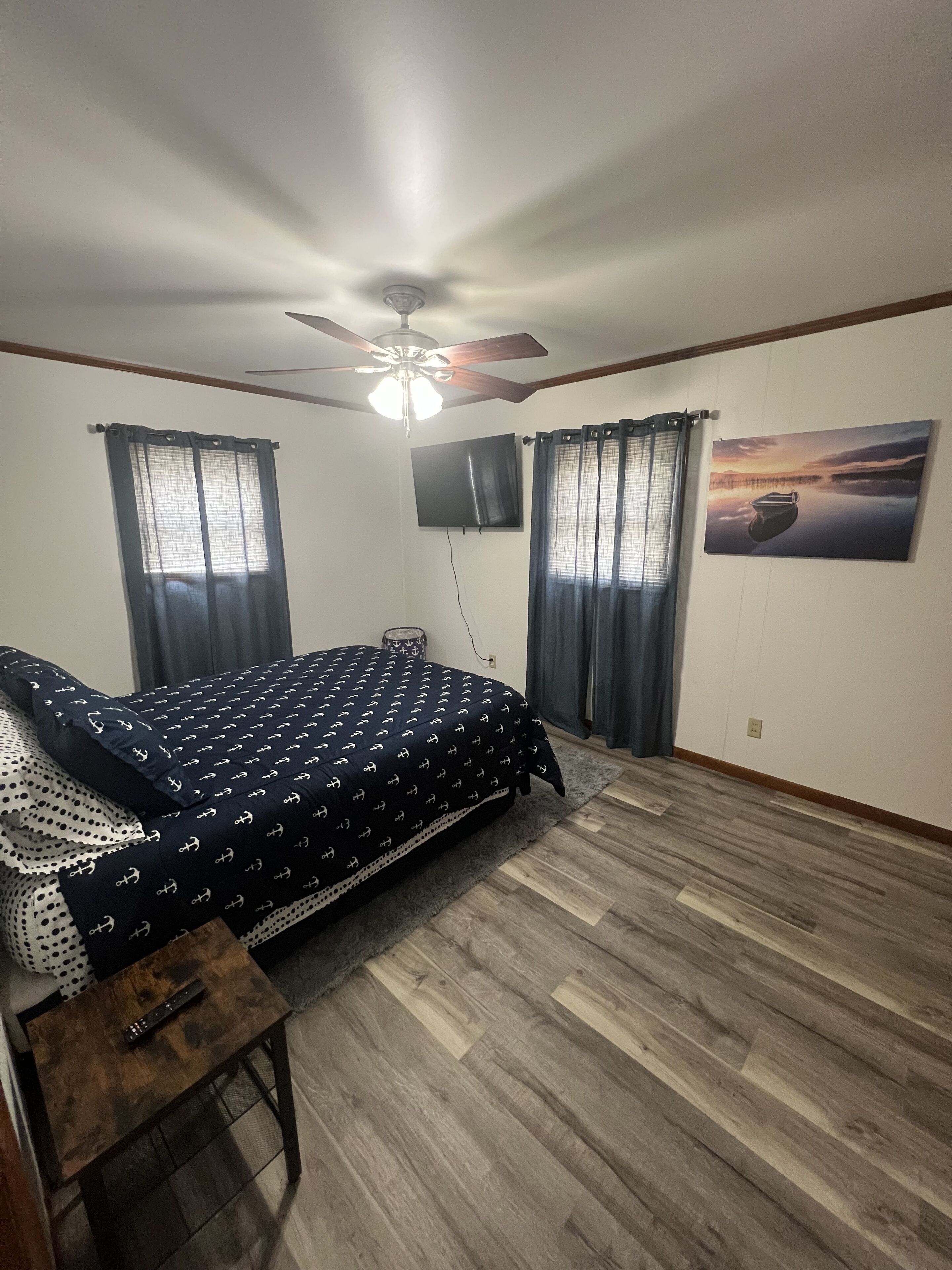 A bedroom with a bed, a ceiling fan, a TV, and a painting on the wall.