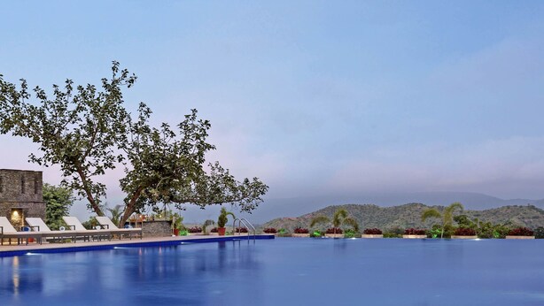 A swimming pool with lounge chairs and a tree. - The Kumbha Residency-Luxury Resort and Spa (Kumbhalgarh)