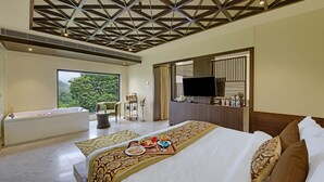 A hotel room with a large bed, a bathtub, a TV, and a view of greenery. - The Kumbha Residency-Luxury Resort and Spa (Kumbhalgarh)