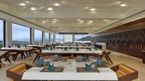A spacious dining area with multiple tables set for guests, large windows offering a view of the landscape, and a modern ceiling design. - The Kumbha Residency-Luxury Resort and Spa (Kumbhalgarh)