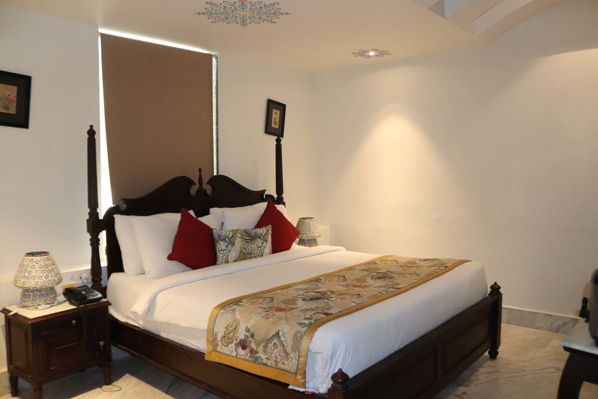 A neatly made bed with a wooden headboard, white bedding, and a decorative throw. There are two bedside tables with lamps and a framed picture on the wall.