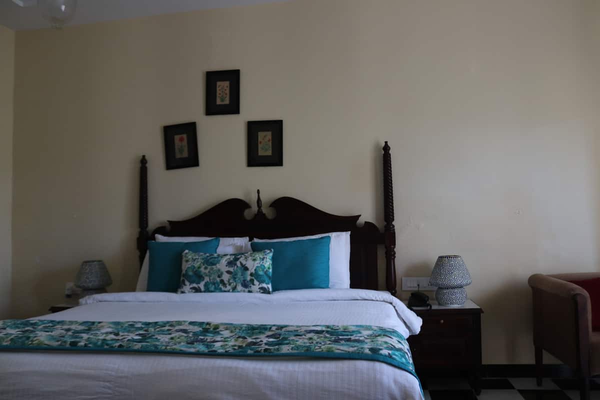 A neatly made bed with a floral-patterned blanket and teal pillows, a wooden headboard, and two framed pictures on the wall.