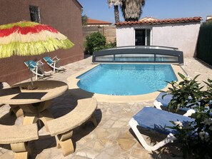 En swimmingpool med solstolar och ett bord i sten.