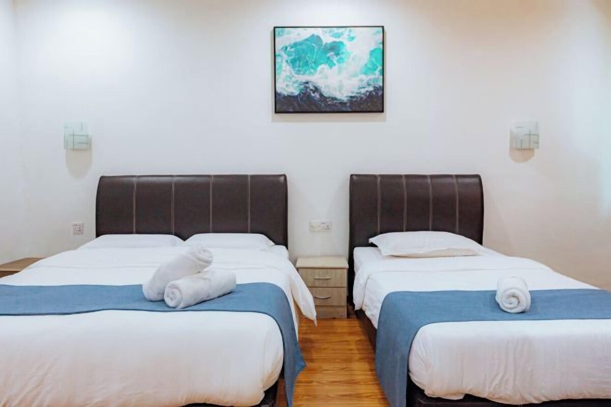 A hotel room with two beds, a wooden floor, a painting on the wall, and a small nightstand between the beds.