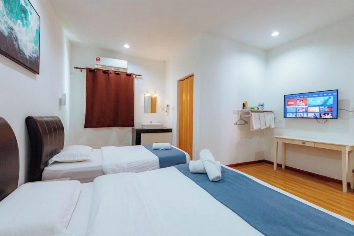 Habitación de hotel con dos camas, un escritorio, una televisión y un baño con cortina de ducha.