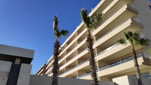 Ett hotell med flera våningar och modern design, med balkonger och en klarblå himmel.