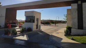 En modern entré till en byggnad med en säkerhetskiosk, en klar himmel och ett välskött trädgårdsområde.