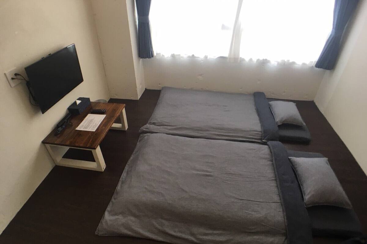 Une chambre avec deux lits, un bureau, une télévision et une fenêtre avec des rideaux.