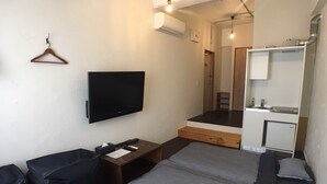 A compact room with a bed, a TV, a small desk, a hanging clothes rack, and a kitchenette. - GOLDEN MILE Hostel (Amami)
