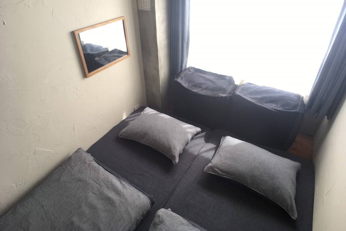 Une petite pièce, de taille modeste, comprenant un lit simple, deux oreillers, un tableau encadré accroché au mur et une fenêtre avec des rideaux.