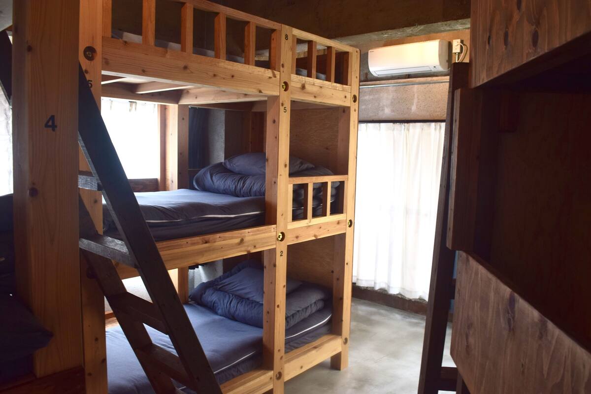 Un lit superposé à trois niveaux, avec des murs en bois et une fenêtre avec des rideaux.