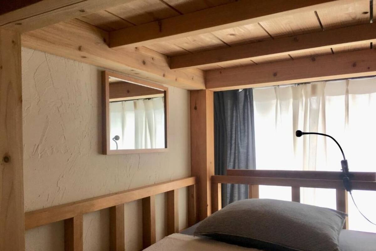 Une pièce aux murs en bois, avec un lit, un miroir et une fenêtre ornée de rideaux.