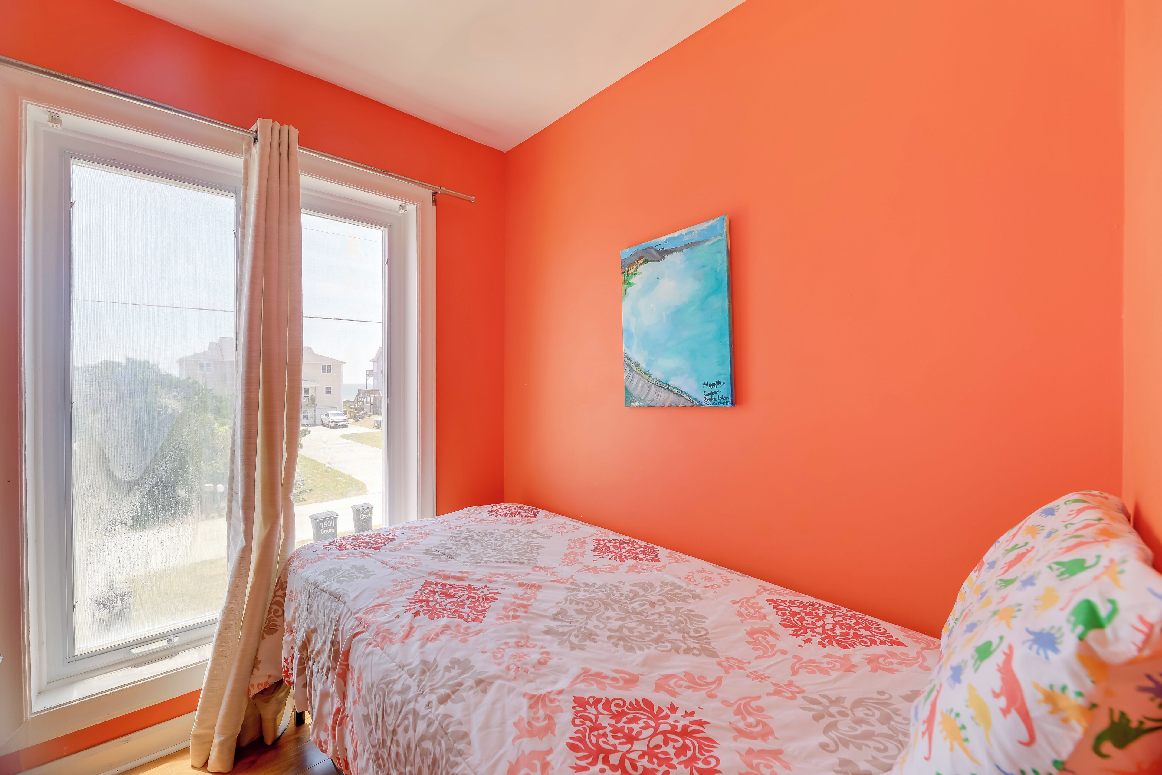 A room with a bed, a window with curtains, and a painting on the wall.