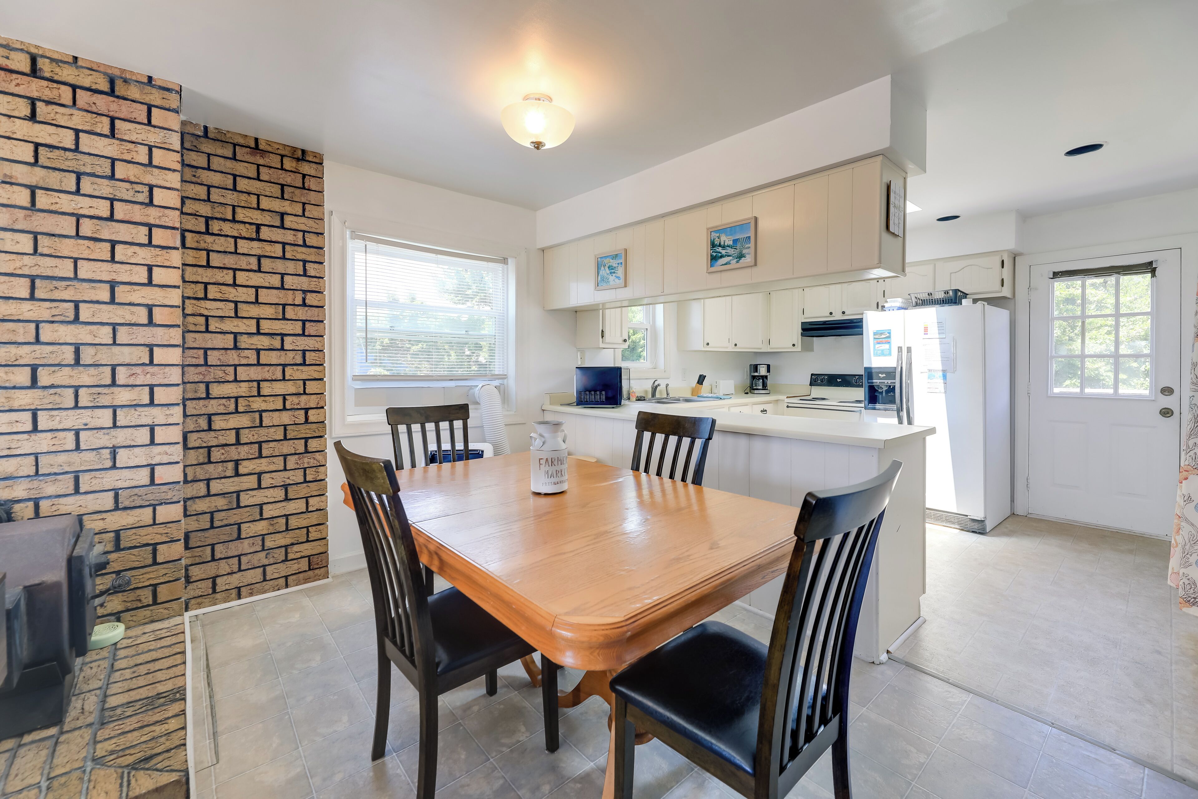 A kitchen with a wooden table and chairs, white cabinets, and a brick accent wall.
