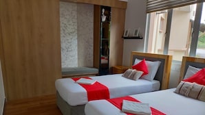 A hotel room with two beds, each with white bedding and red accents, a wooden floor, a built-in bench, and a window with blinds. - Seri Bayu Resort (Sungai Pelek)
